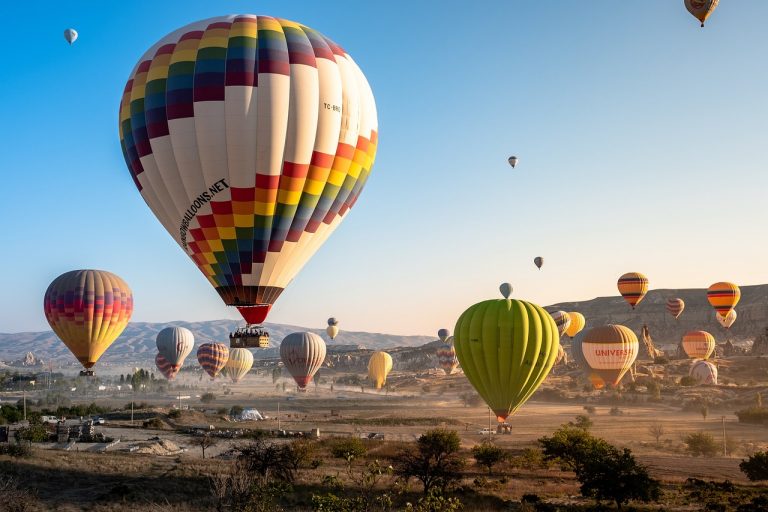 A scenic view of Cappadocia's landscape with multiple hot air balloons floating in the clear blue sky during early dawn